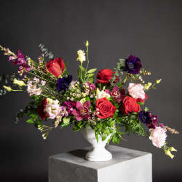 Mixed bouquet of red roses, purple blooms, and pale pink flowers in a white vase