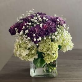 Purple and green hydrangea bouquet in a clear square vase