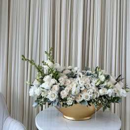 Large white floral arrangement in a gold bowl on a round table