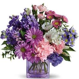 Mixed bouquet of purple, pink, and white flowers in a purple glass vase
