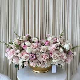 Large pastel pink and white floral arrangement in a gold bowl.