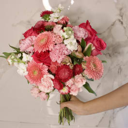 Handheld bouquet of pink and red flowers with white accents