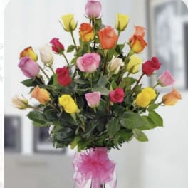 Tall bouquet of multicolored roses in a clear vase with a pink ribbon