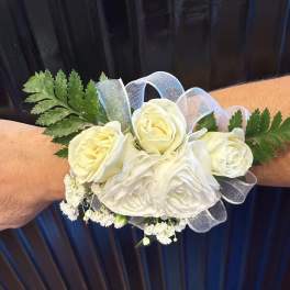 White rose wrist corsage with sheer ribbon accents worn on an arm.