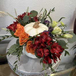 Floral arrangement around a white pumpkin centerpiece with orange and red blooms