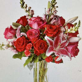 Tall arrangement of red and pink roses, lilies, carnations, and snapdragons in a clear glass vase.