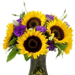 Medium bouquet of bright yellow sunflowers and purple blooms in a green glass vase