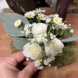 Small wedding boutonniere with white roses, tiny white daisies, and filler blooms held in a hand