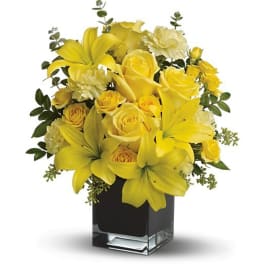 Yellow lilies, roses, and carnations arranged in a black rectangular glass vase
