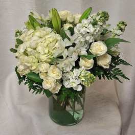 White and cream roses, hydrangeas, lilies, and stock arranged in a clear glass cylinder vase