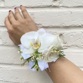 White floral wrist corsage with ribbon on a person's wrist