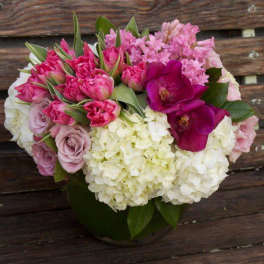 Low round bouquet of white hydrangeas, pink roses and tulips, and purple orchids in a clear glass vase