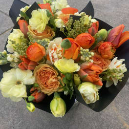 Bouquet of orange, cream, and pale yellow flowers wrapped in black paper