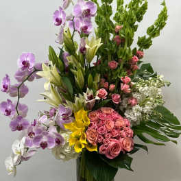 Tall mixed bouquet with orchids, roses, lilies, and hydrangeas in a glass vase