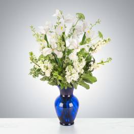 Arrangement of white irises and white stock in a deep blue glass vase
