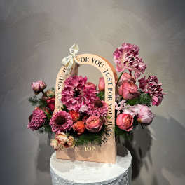 Pink and purple floral arrangement in a gift bag with a ribbon handle