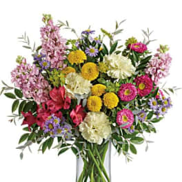 Mixed bouquet of pink, yellow, white, and purple flowers in a clear glass vase