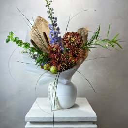 Tall bouquet of chrysanthemums and blue delphinium in a white vase