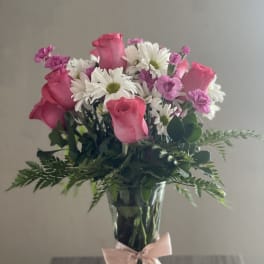 Pink roses and white daisies in a clear glass vase with a pink ribbon