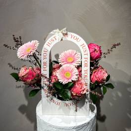 Pink gerbera daisies and roses arranged in a white gift bag with a ribbon handle.