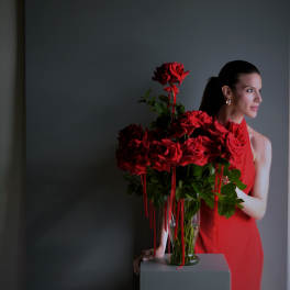 Red roses in a glass vase beside a woman in a red dress