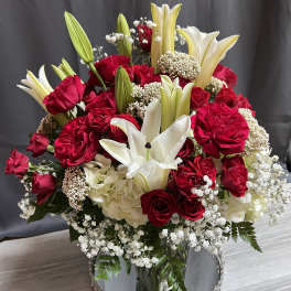 Red roses and white lilies in a mirrored vase with baby's breath