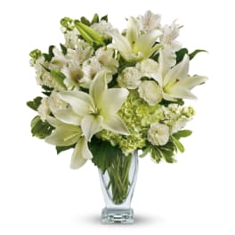 White lilies and mixed white flowers in a clear glass vase