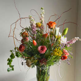 Tall mixed flower arrangement in a clear glass vase with orange and pink blooms