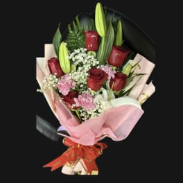 Bouquet of red roses, pink carnations, and white lilies wrapped in pink paper