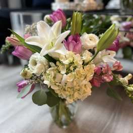 Mixed bouquet of white lilies, hydrangeas, and pink tulips in a clear glass vase