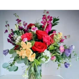 Mixed bouquet of roses, orchids, and purple blooms in a glass vase