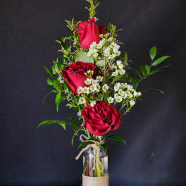 Three red roses in a glass bottle vase with white filler flowers