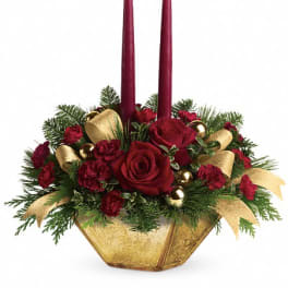 Low centerpiece of red roses and carnations with evergreens in a gold bowl and two tall burgundy candles.