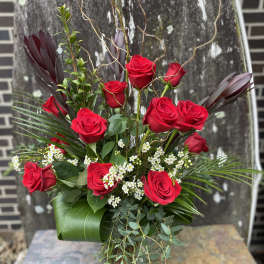 Red roses arranged in a glass vase with white filler flowers