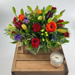 Colorful mixed flower arrangement in a wooden box with a candle beside it