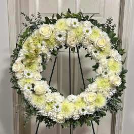 White floral wreath on a black stand with roses and mums