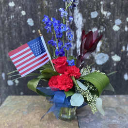 Red and blue floral arrangement in a glass vase with an American flag