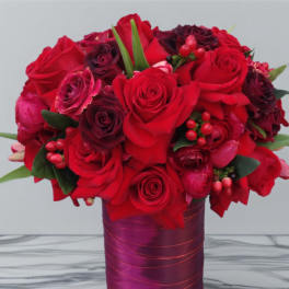 Red roses and dark burgundy blooms in a purple vase