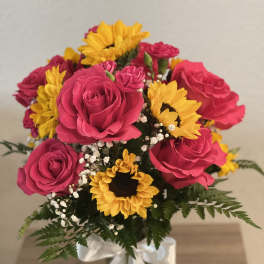 Bouquet of pink roses and yellow sunflowers in a glass vase with a white ribbon