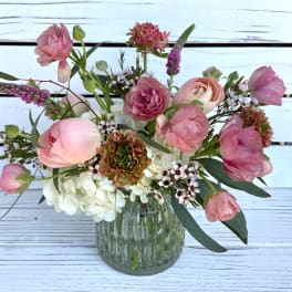 Small glass vase with pink ranunculus and mixed flowers in a loose, airy arrangement
