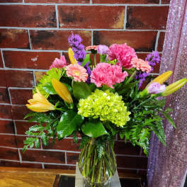 Mixed bouquet of pink, purple, and yellow flowers in a glass vase