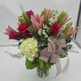 Bouquet of pink lilies, red roses, and pale hydrangea in a glass vase