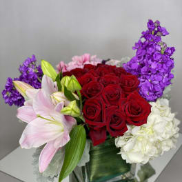 Bouquet of red roses, pink lilies, purple stock, and white hydrangea in a glass vase
