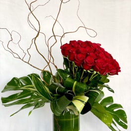Red roses arranged in a tall glass vase with broad tropical leaves