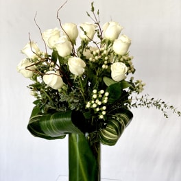 White roses arranged in a tall glass vase with green foliage