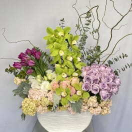 Mixed floral arrangement in a white rectangular vase with orchids and roses
