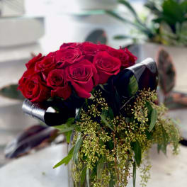 Red roses arranged in a clear glass vase with trailing greenery