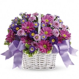 Purple and pink daisy bouquet in a white wicker basket with lavender ribbon