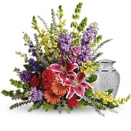 Mixed bouquet with lilies, roses, and purple flowers beside a silver urn