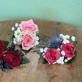 Three small rose corsages with baby's breath on a wooden surface